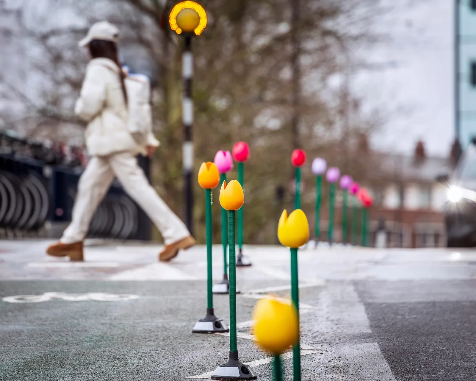 A person in light-colored clothing walks on a path lined with colorful tulip-shaped bollards.